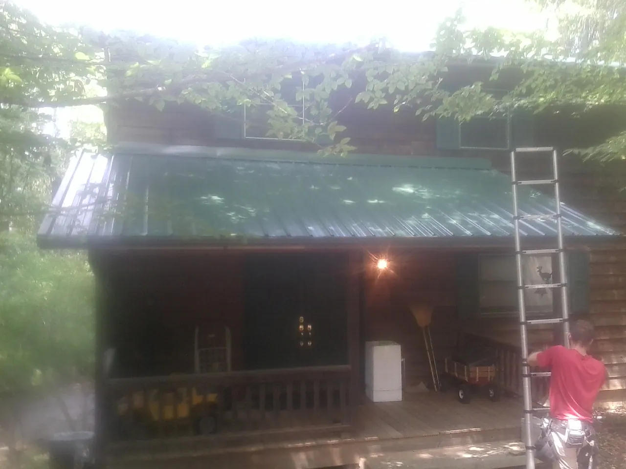 Worker on a ladder at the green porch roof of a wooded cabin in Madison